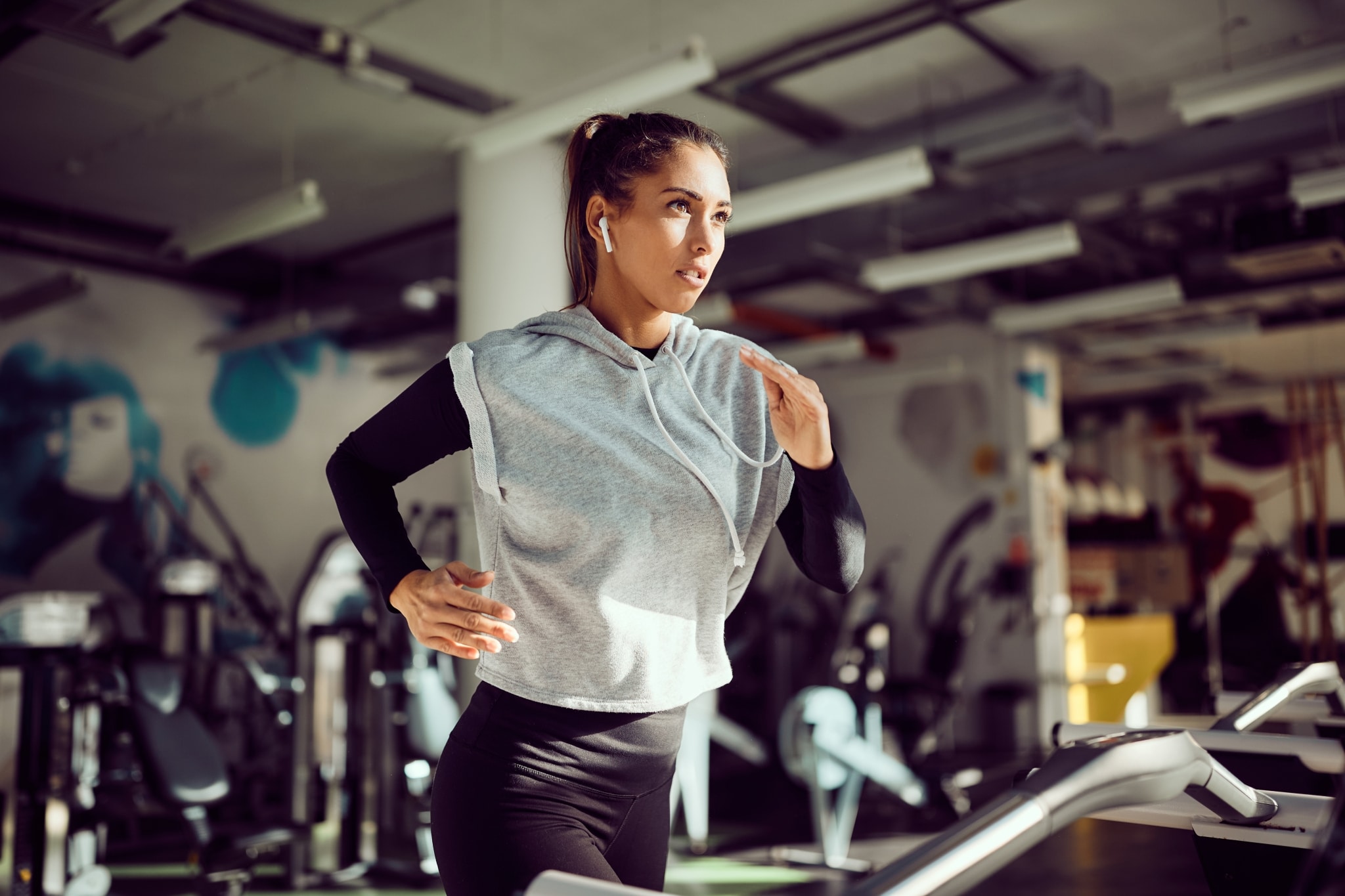 Junge Frau im grauen Trainingsgewand und Kopfhörer läuft auf einem Laufband in einem Fitnessstudio
