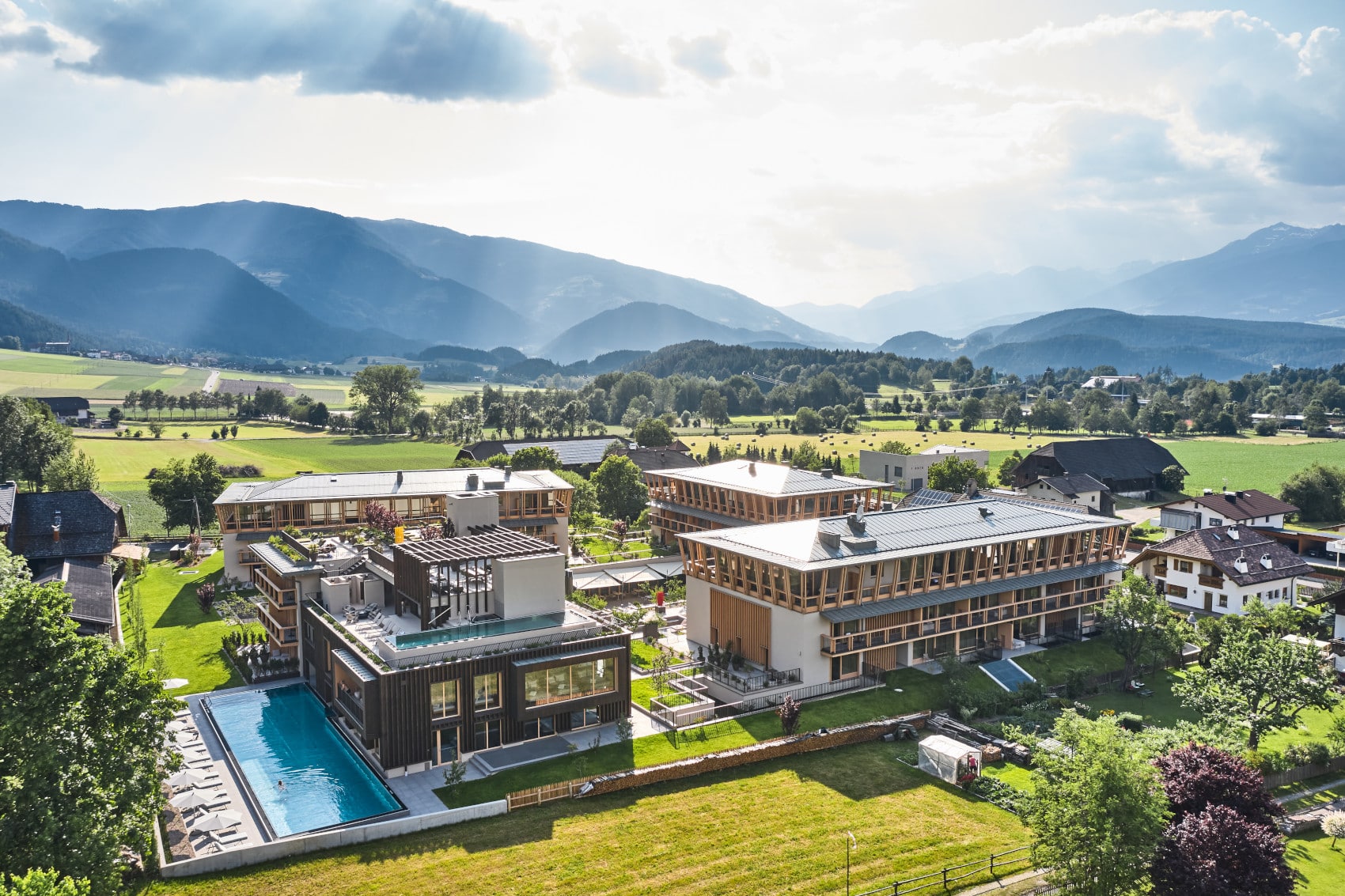 Das Falkensteiner Hotel Kronplatz bestehend aus mehreren Gebäuden in mitten grüner Wiesen und vor einer Bergkulisse