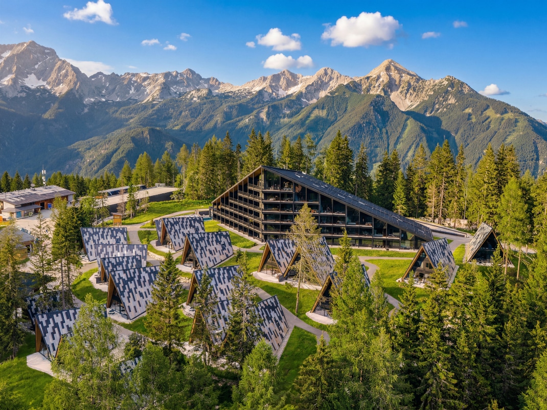 Blick auf eine Challet Häuser Ansammlung inmitten von Bäumen vor einer Bergkulisse